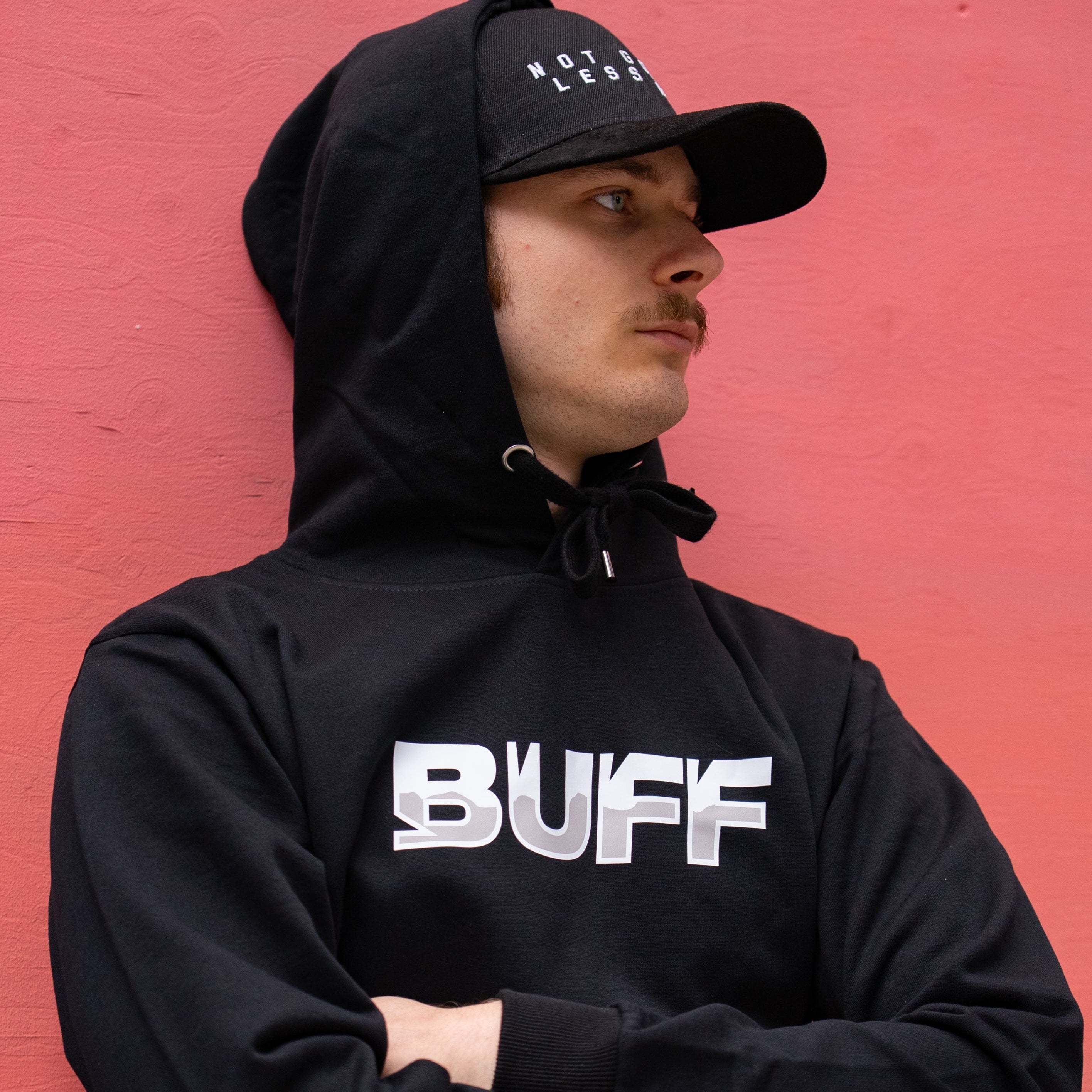 Person wearing a black hoodie with 'BUFF' logo and black cap against a red background