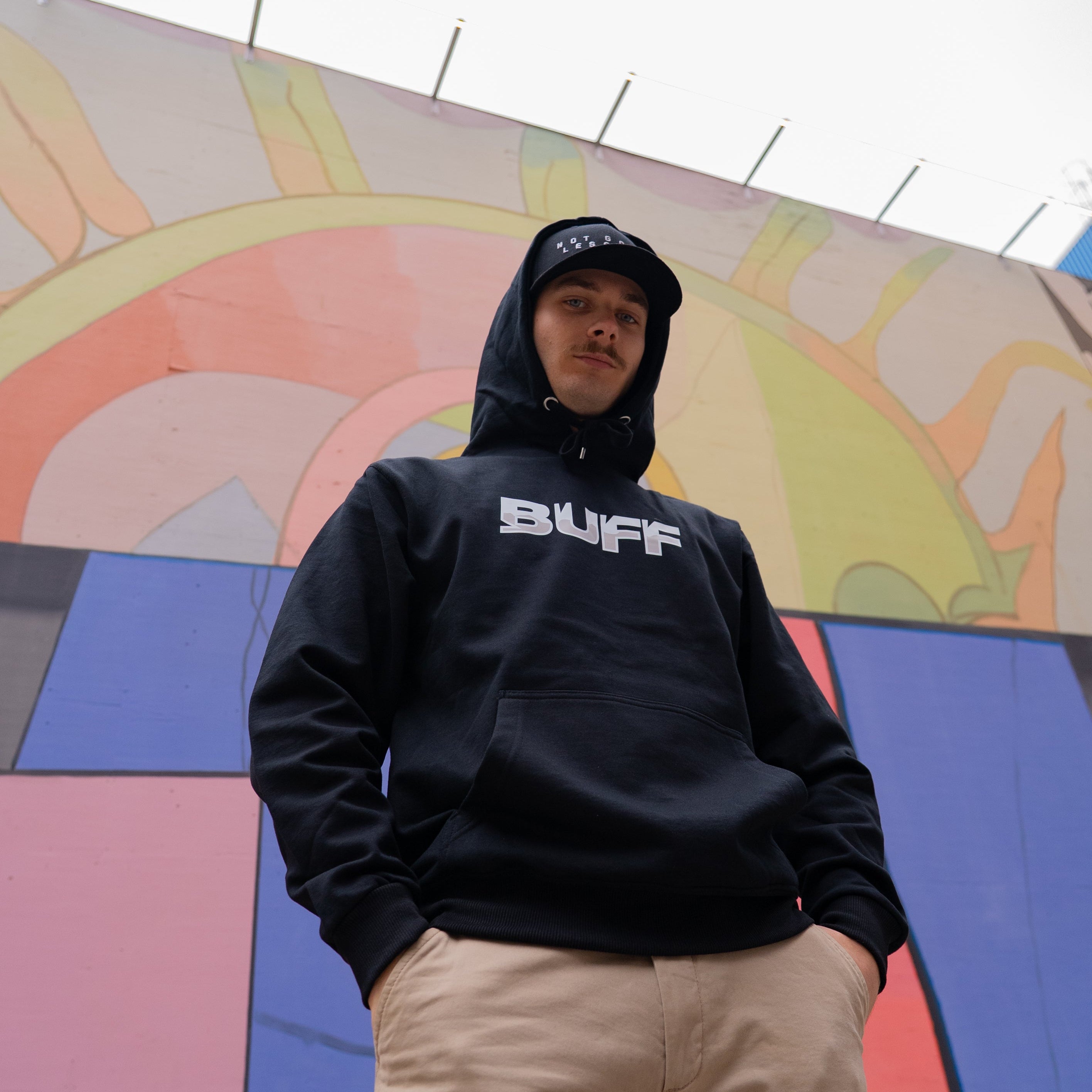 Person wearing a black hoodie with 'BUFF' logo in front of a colorful mural.