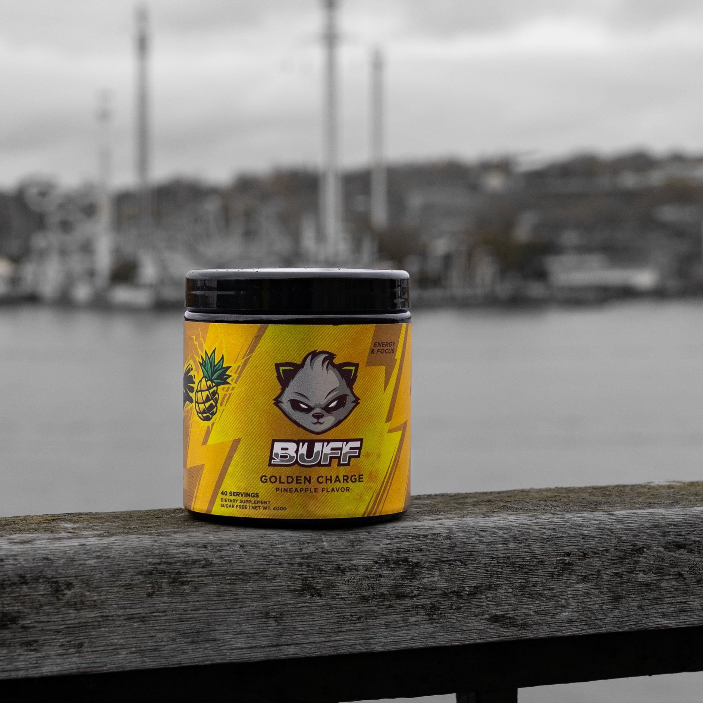 Yellow and black container labeled 'BUFF' on a wooden surface with a blurred waterfront background